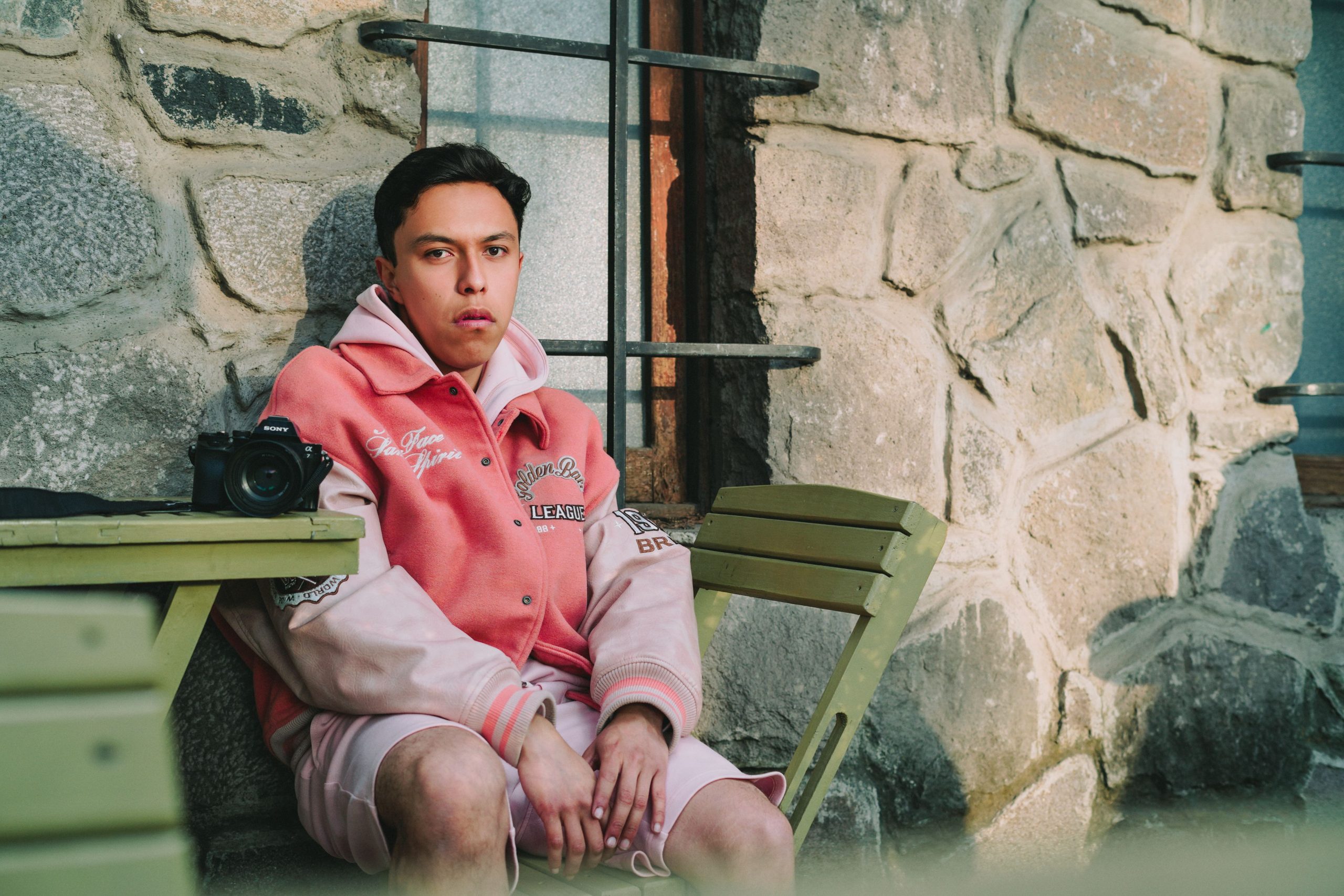 Homme en bomber rose assis en extérieur.