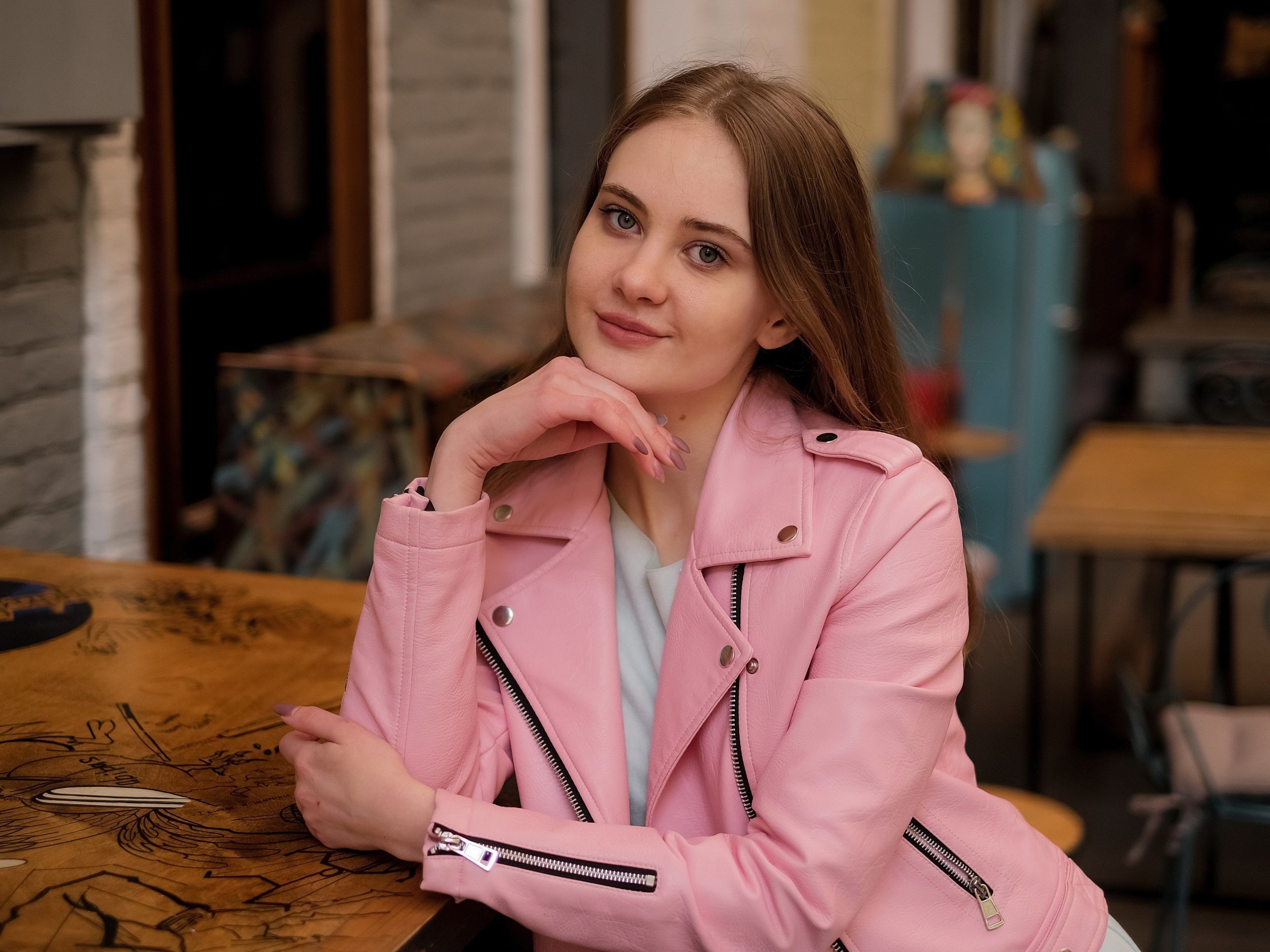 Femme en veste rose cuir posant en café.